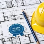 An ISO 9001 certification seal on a construction blueprint background with symbols representing building codes and quality craftsmanship in the construction industry.