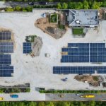 Aerial view of a sustainable construction site featuring solar panels, green roofs, and native landscaping, situated near green spaces and public transit.