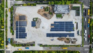 Aerial view of a sustainable construction site featuring solar panels, green roofs, and native landscaping, situated near green spaces and public transit.