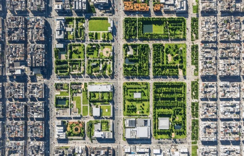 Aerial view of an urban district with a split-screen comparison showing before and after revitalization. The before side depicts aging infrastructure and sparse greenery, while the after side features modern buildings, lush green areas, and bustling activity.