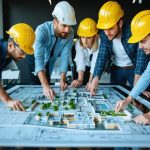 "A diverse team of construction professionals, including architects, contractors, and project managers, collaborating around a digital table with architectural plans and BIM models, highlighting teamwork and integrated project delivery."