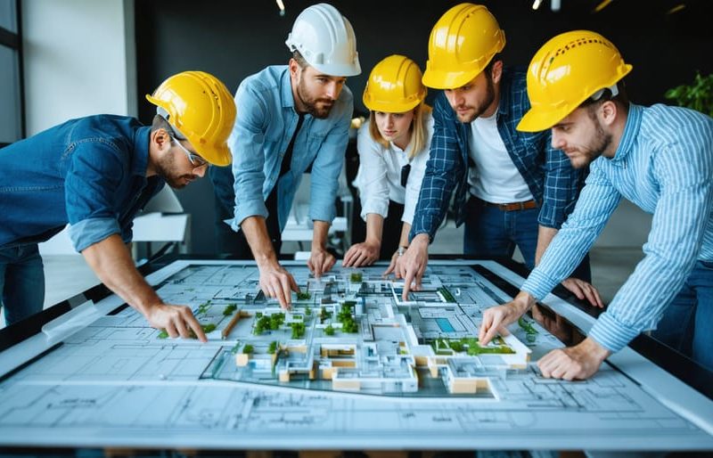 "A diverse team of construction professionals, including architects, contractors, and project managers, collaborating around a digital table with architectural plans and BIM models, highlighting teamwork and integrated project delivery."