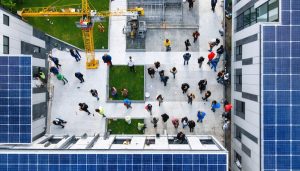 A bird's eye view of a sustainable construction site with multiple stakeholder teams collaborating amid solar panels and green spaces.