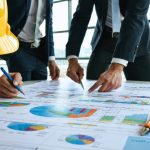 Construction professionals engaged in a risk management meeting, examining blueprints and risk matrices in a modern office setting.